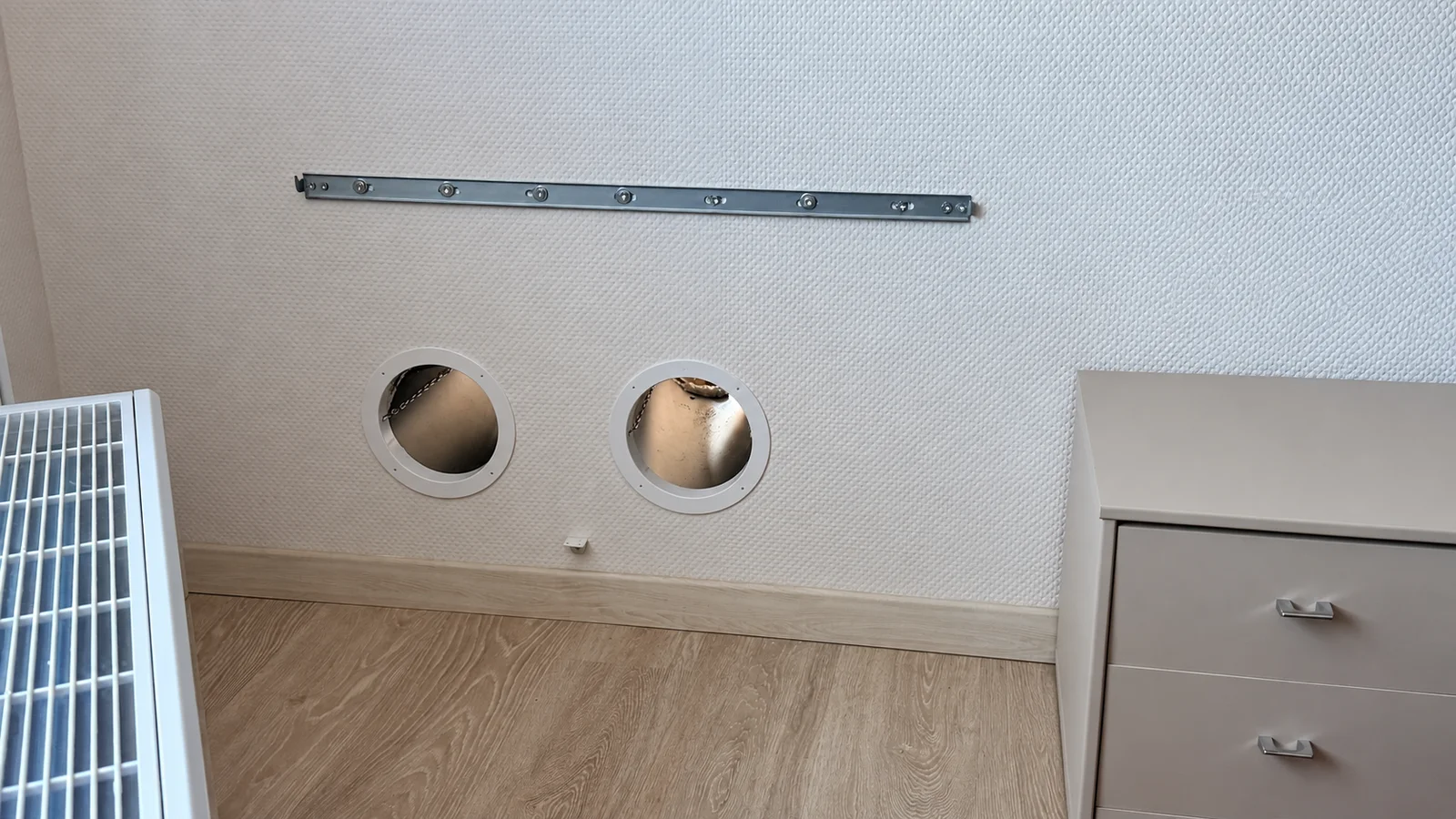 Deux traversées circulaires dans un mur et un rail de fixation, avec un appareil partiellement visible à gauche.